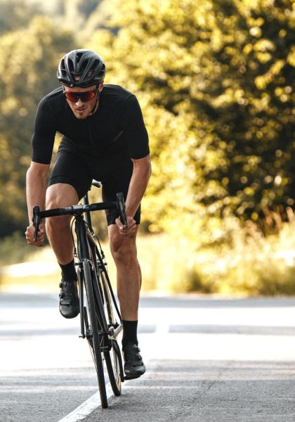 Ciclista in movimento su strada alberata, indossa casco e occhiali.