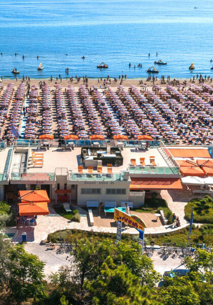 Spiaggia affollata con ombrelloni colorati e ristorante sul mare.