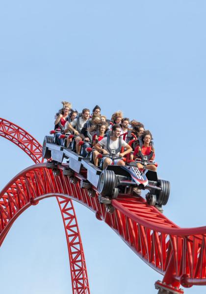 Persone su montagne russe rosse in un parco divertimenti.