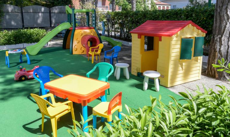 Area giochi per bambini con scivolo e casetta colorata all'aperto.