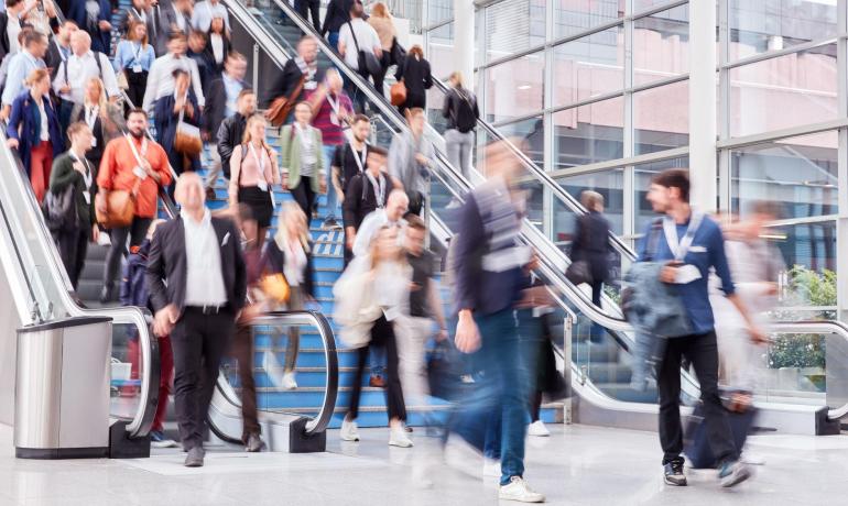 Folla di persone che camminano in un edificio con scale mobili.