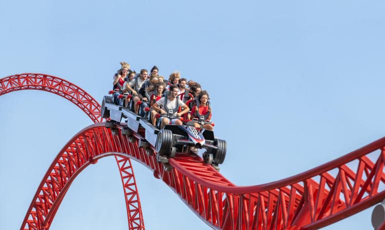 Persone su montagne russe rosse in un parco divertimenti.