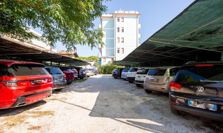 Parcheggio auto all'aperto con tettoie e alberi.